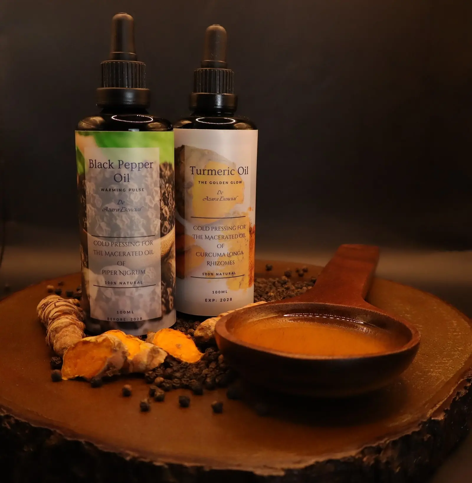 products shot for bottles of oils of black pepper oil and turmeric oil with natural ingredients and wooden spoon full of the oils with black background and wooden base BY azara natural