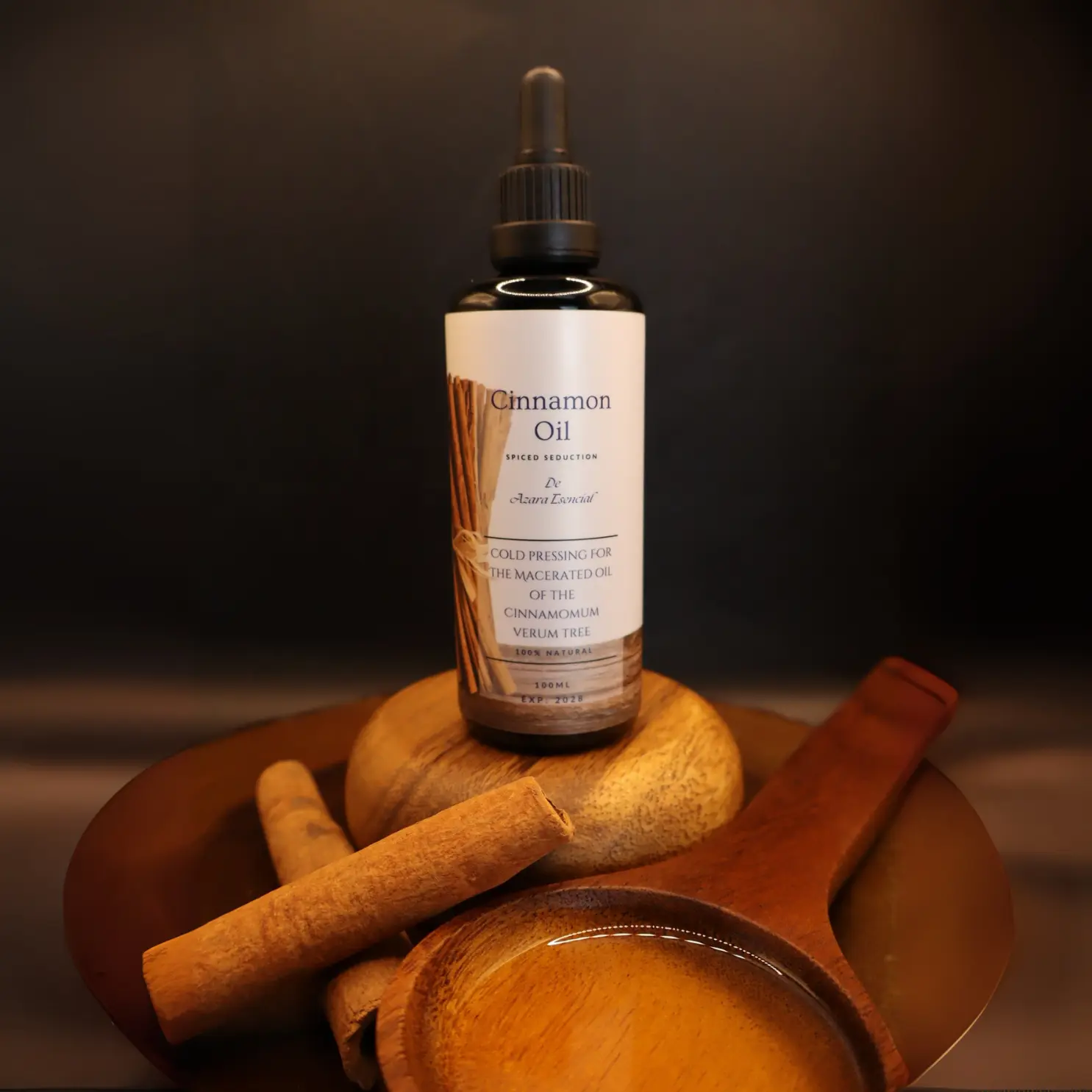 cinnamon-oil BY azara natural product image with black background with wooden spoon and some natural cinnamon sticks