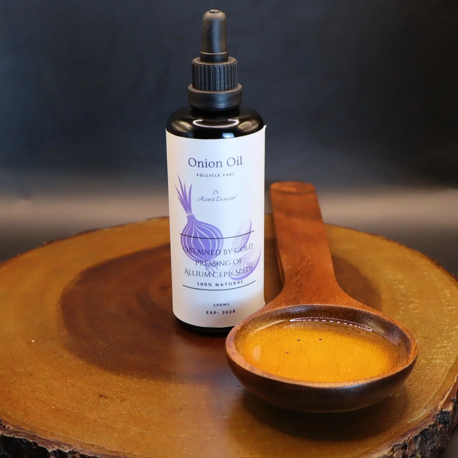 Product shot with black background for the bottle of onion oil with a wooden spoon full of the oil BY azara natural