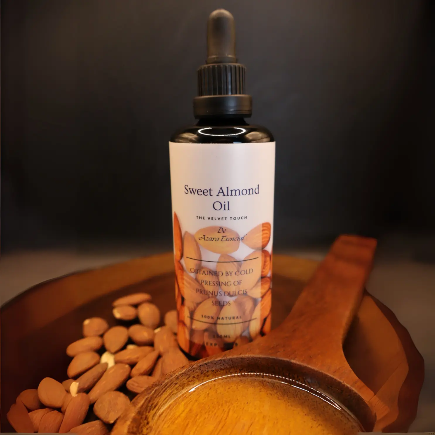Sweet almond oil bottle BY azara natural professional product shot with black background and wooden spoon full of the oil and some natural almonds all of them on a circular wooden base